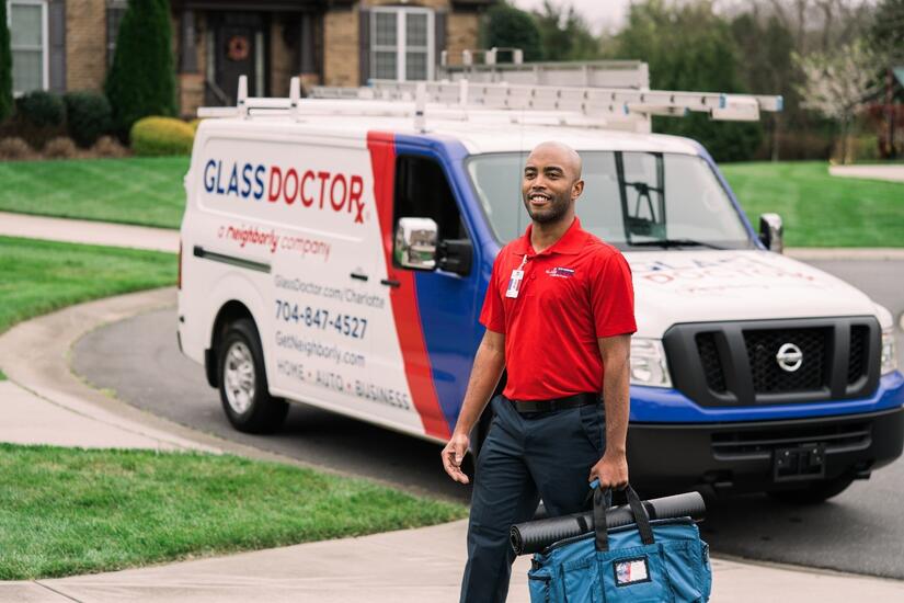 Man holding a bag and standing in front of van with Glass Doctor written on it going towards a home to discuss door closer repair service